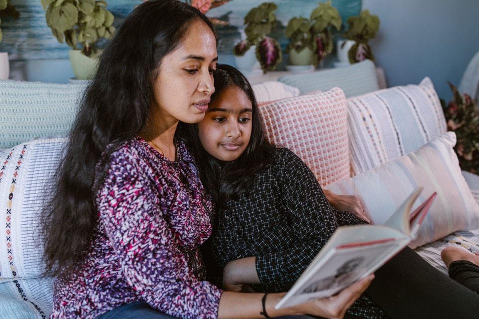 An Indian mother and daughter reading a book together at home